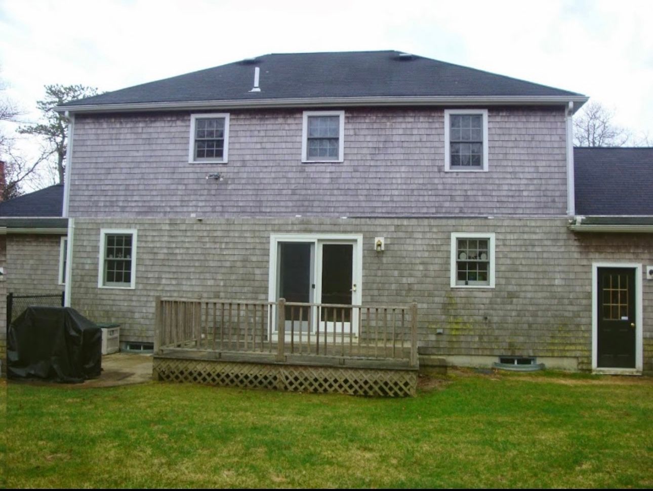 Two-story house with gray shingle siding, a wooden deck, a sliding glass door, and a grassy backyard.