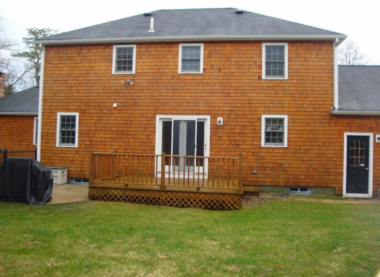 A two-story wood-shingled house with a backyard deck, sliding glass door, and a black exterior door.