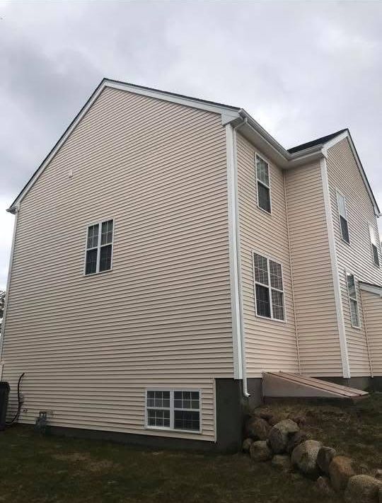 Exterior side view of a two-story beige house with white trim, multiple rectangular windows, and a rock-lined foundation.