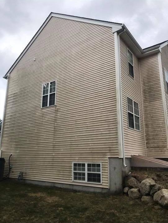 A multi-story house with light beige vinyl siding showing significant streaking and dirt buildup on an overcast day.