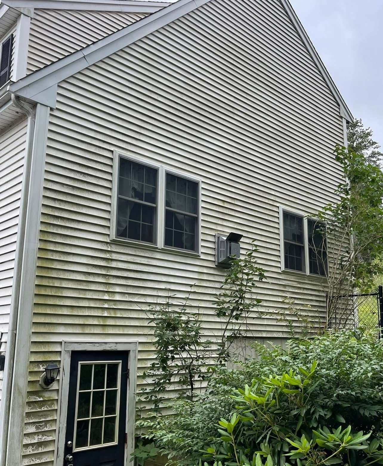 A two-story house exterior with light-colored, dirty horizontal siding, a dark blue door, and multiple windows.