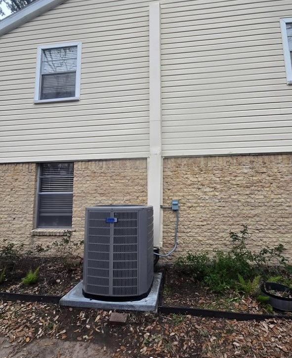 Outdoor air conditioning unit beside beige vinyl siding and stone veneer on a house exterior.