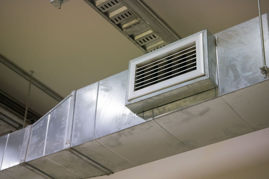 Ceiling-mounted metal HVAC duct with a rectangular air vent in an industrial interior
