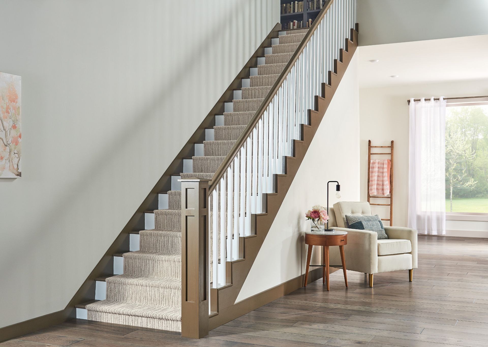 Modern living room with a carpeted staircase, white railing, and armchair by a bright window.