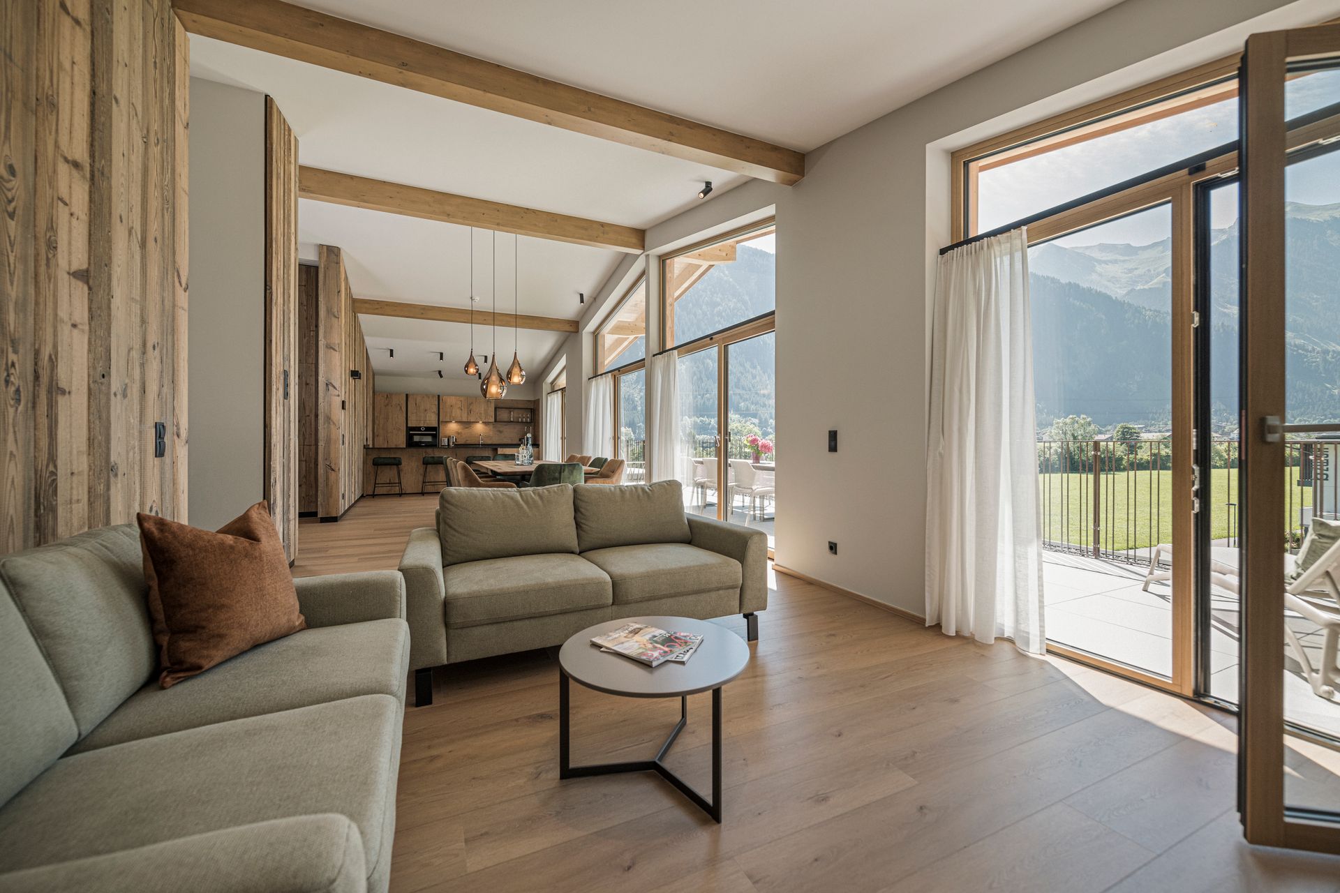 Bright modern living room with beige sofas, wood floors, and large windows opening to a mountain view