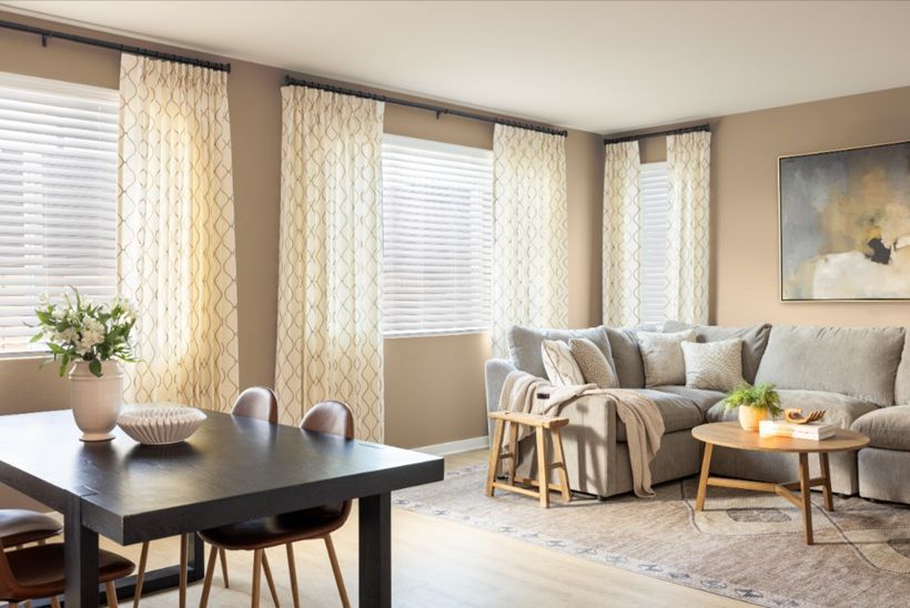 Bright living room with beige sofa, coffee table, large windows, and a dining table by the wall.