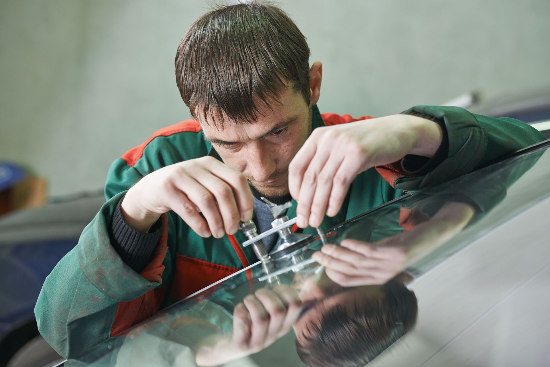 Technician adjusting a small metal part on a reflective surface, wearing a green jacket with red trim.