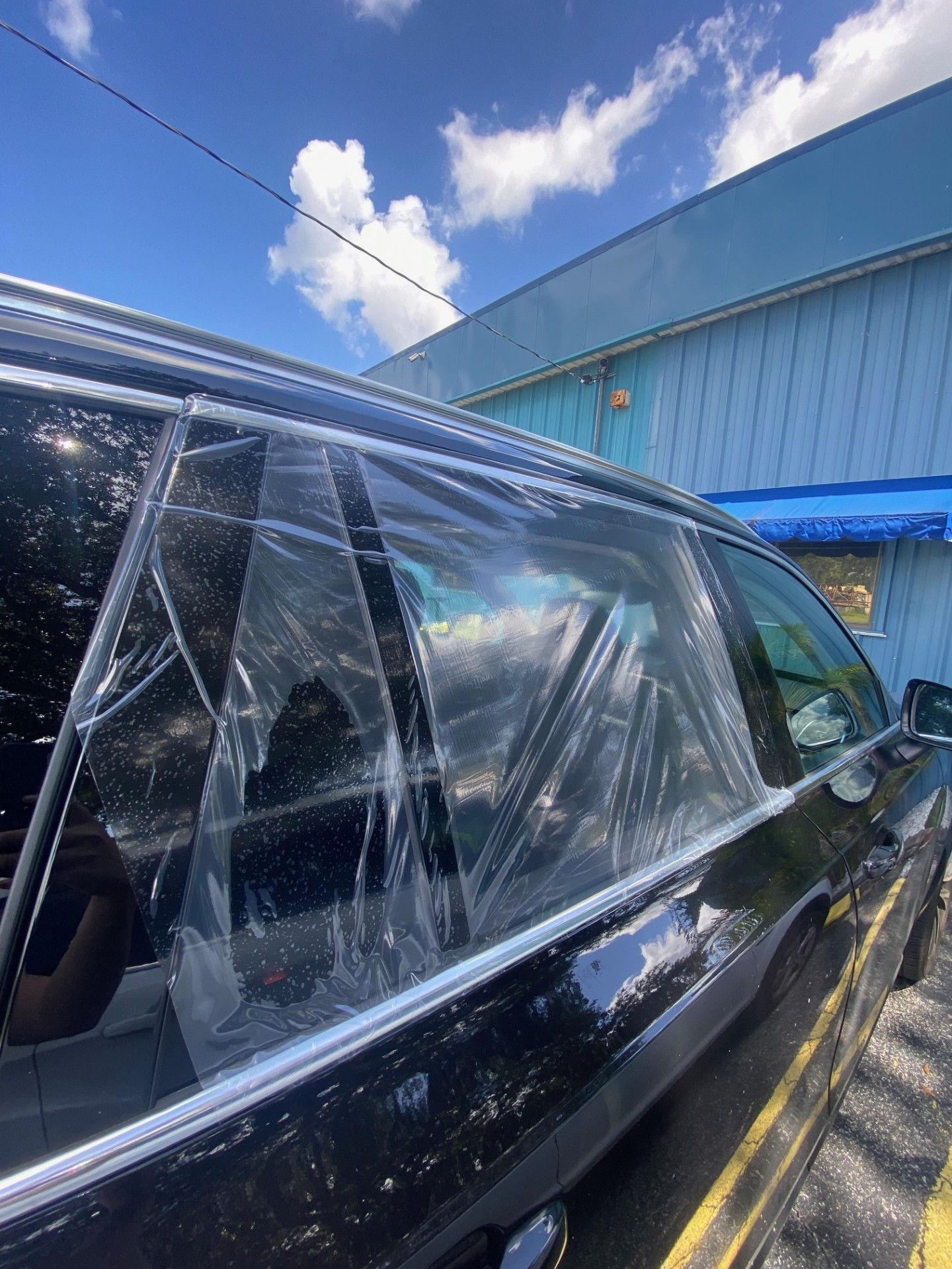 Black car with cracked side windows parked beside a blue building under a sunny sky