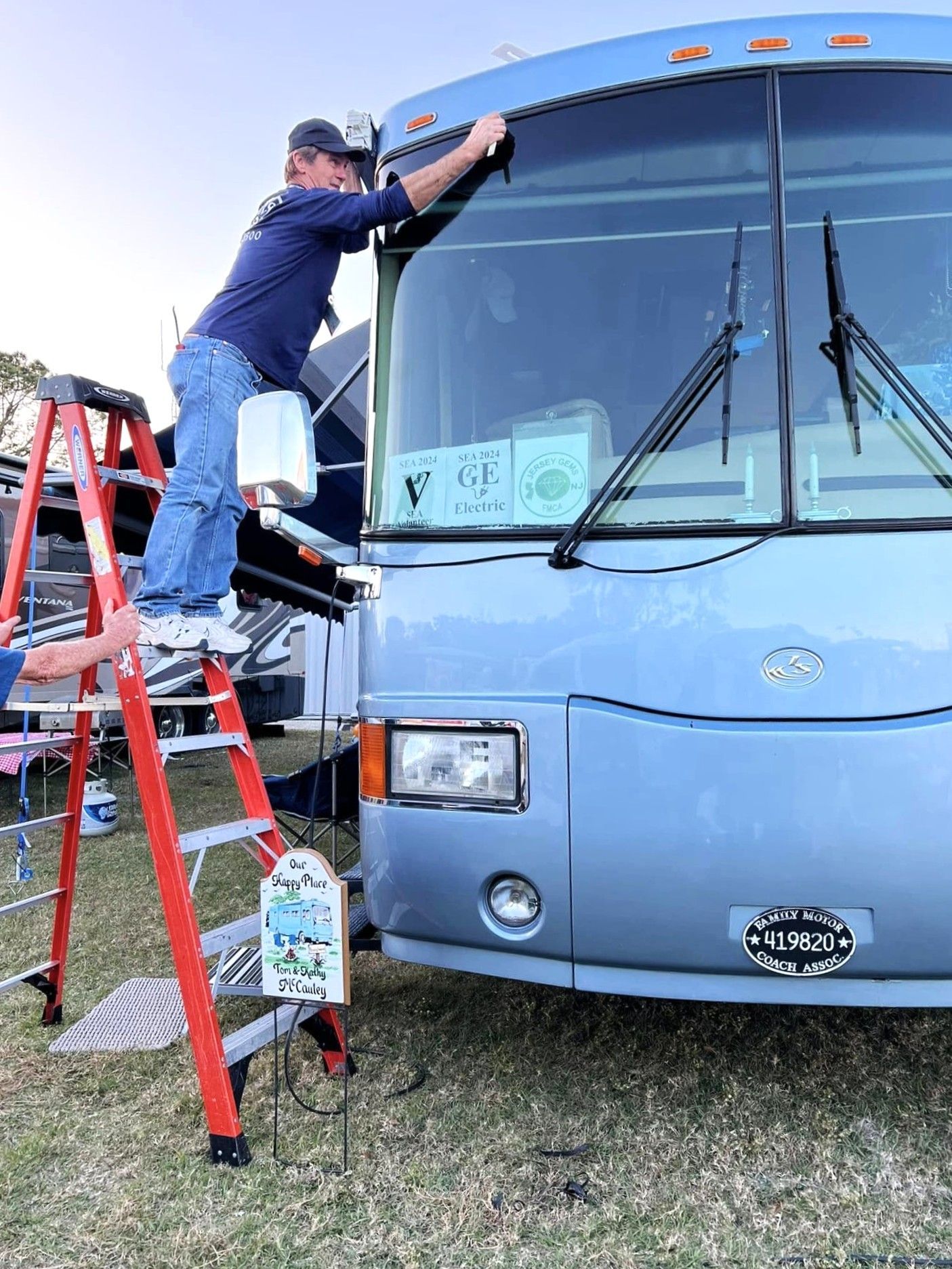 Worker on red ladder cleaning the windshield of a blue bus outdoors