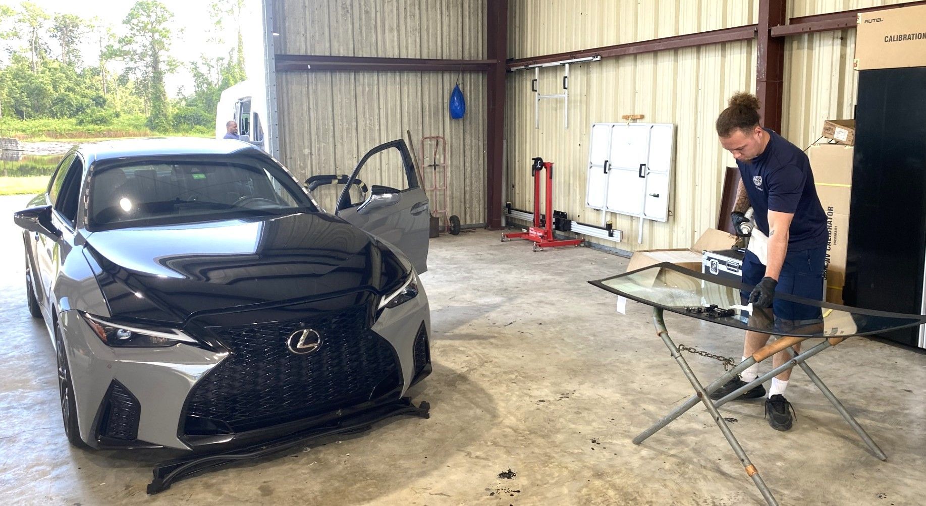 Black sedan in a garage while a man works on a folding ironing board nearby.