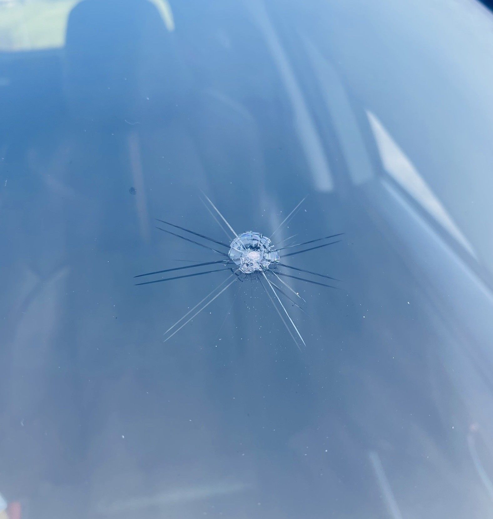 Cracked car windshield with a small impact point and spiderweb radiating cracks.