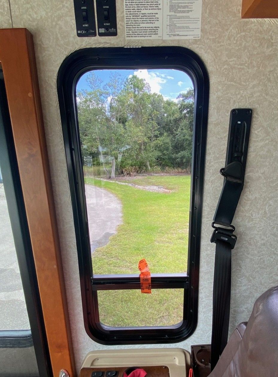 View through a train door window of a grassy park with trees and a curving path.