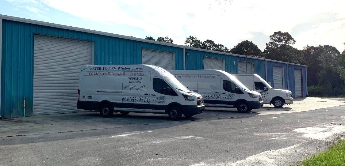 Three white delivery vans parked outside a blue industrial building on a sunny day