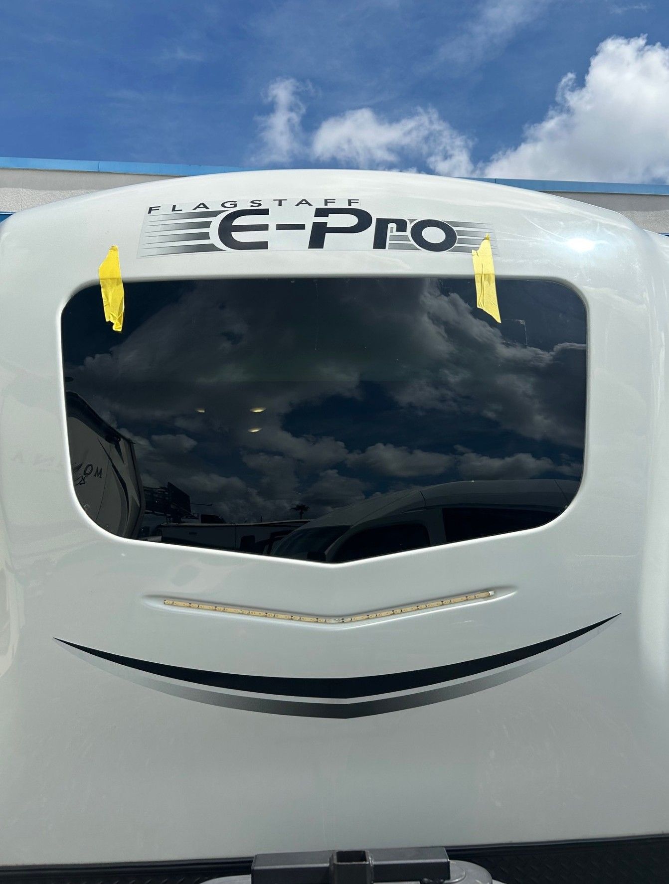 White e-PRO vehicle rear with tinted window and smiling decal under blue sky with clouds