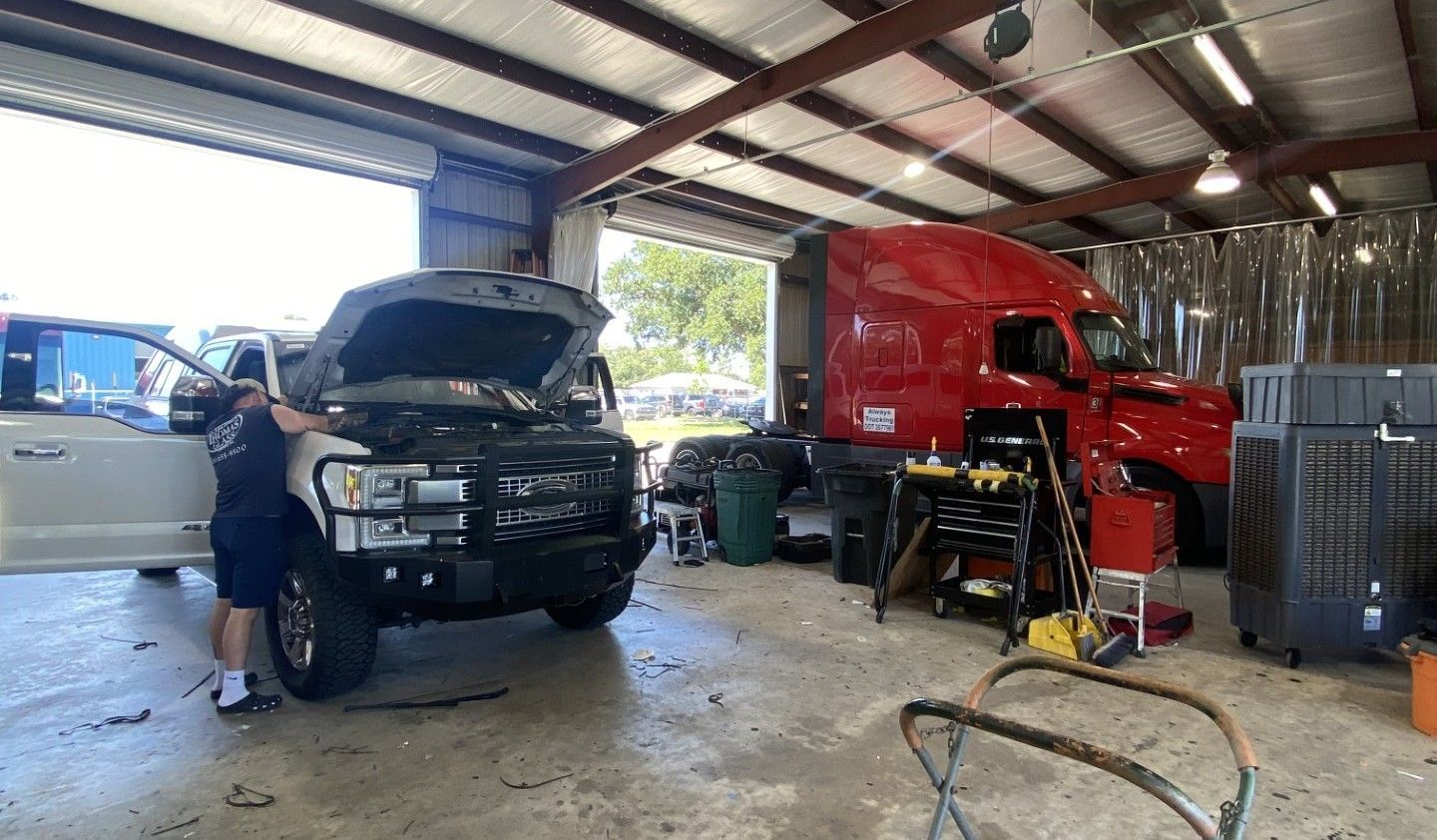 Mechanic working beside black and red semi trucks inside a repair shop