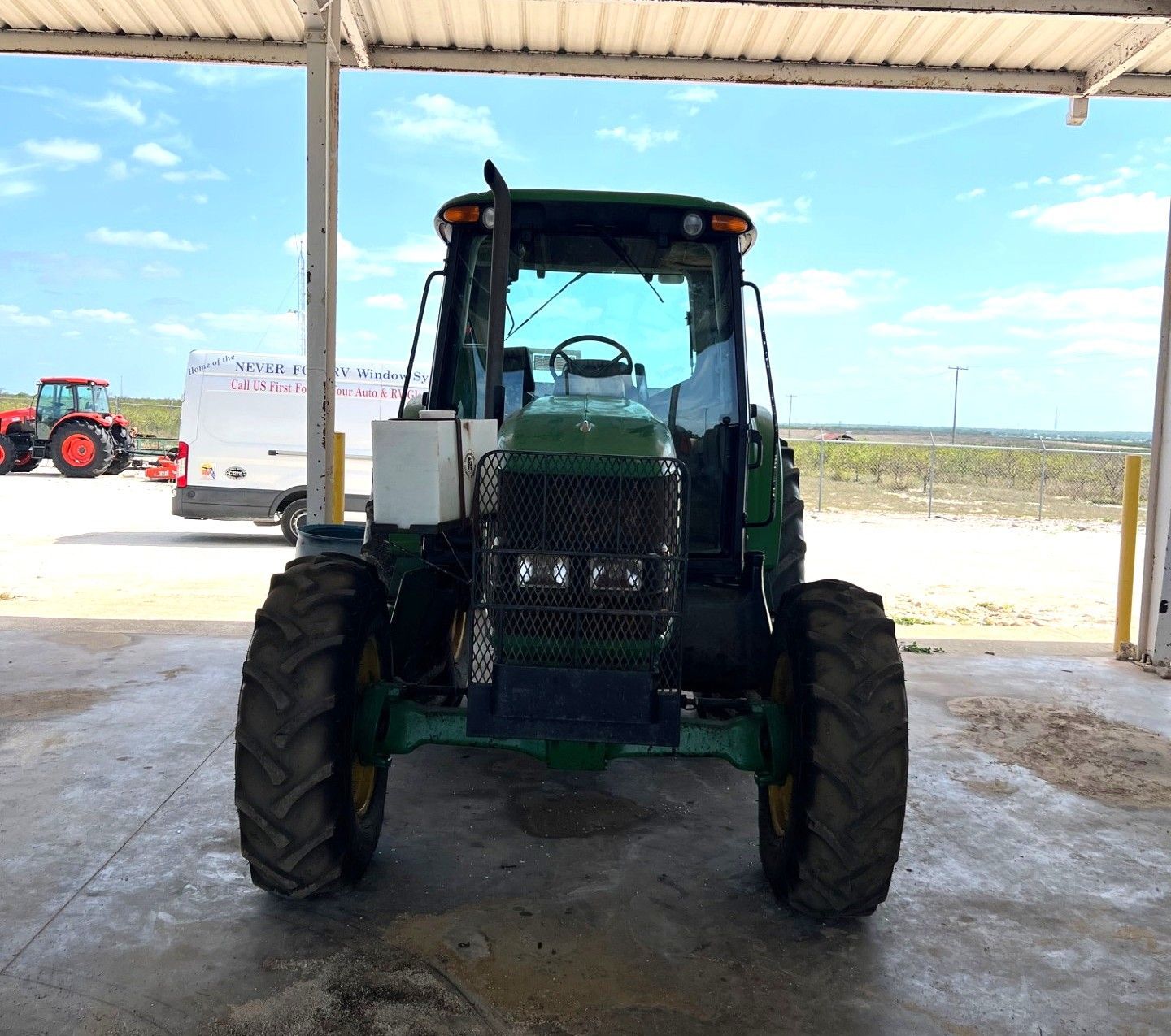 Green tractor parked under a shed at a farm, facing the camera.
