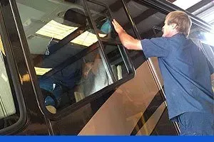 A technician adjusts a large glass window on the side of a parked motorhome.