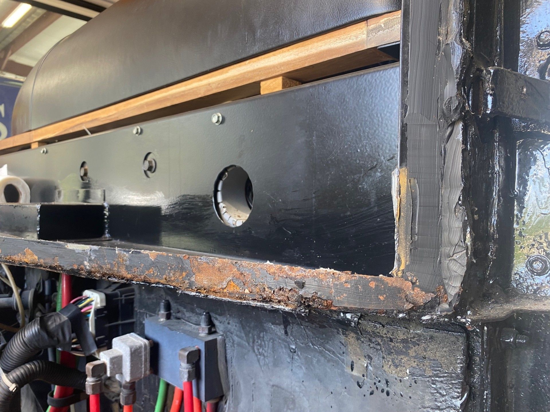 Close-up of a black metal machine panel with a circular hole and rust along the lower edge.