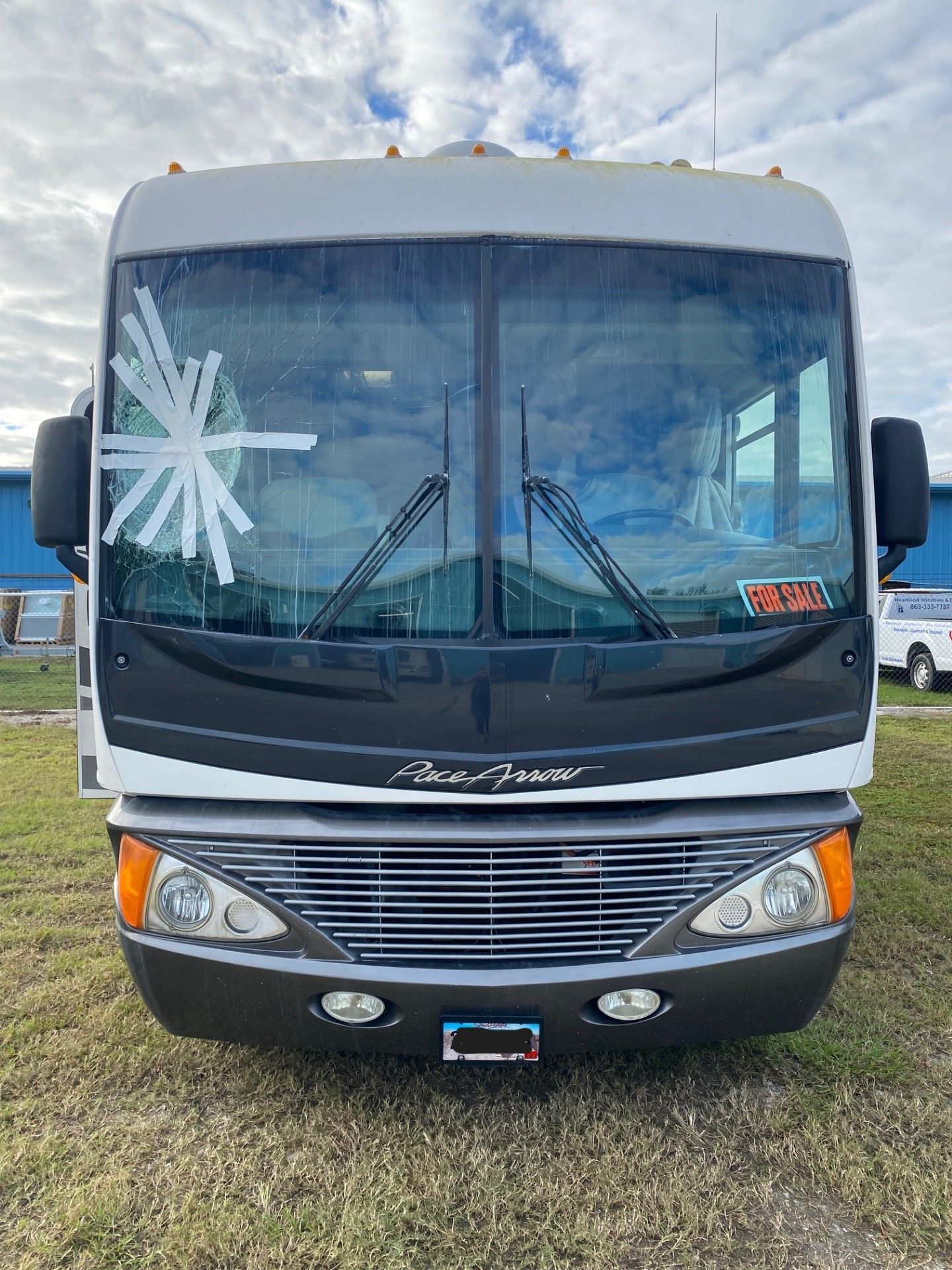 Front view of a gray tour bus parked on grass under a cloudy sky