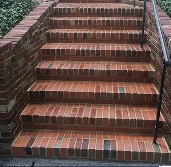 Brick staircase with brick walls and a metal handrail.