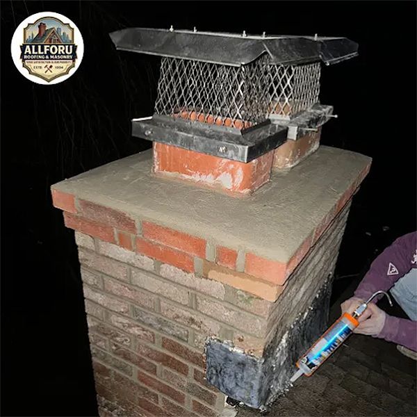 Brick chimney with cap, person sealing metal flashing with caulk.