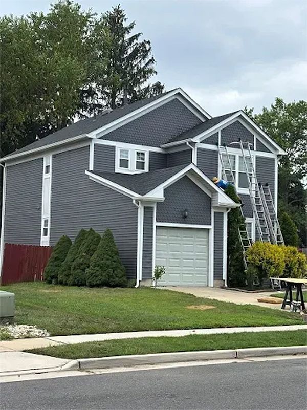 House with dark gray siding, white trim, and a garage. Ladders lean against the house; painting is in progress.