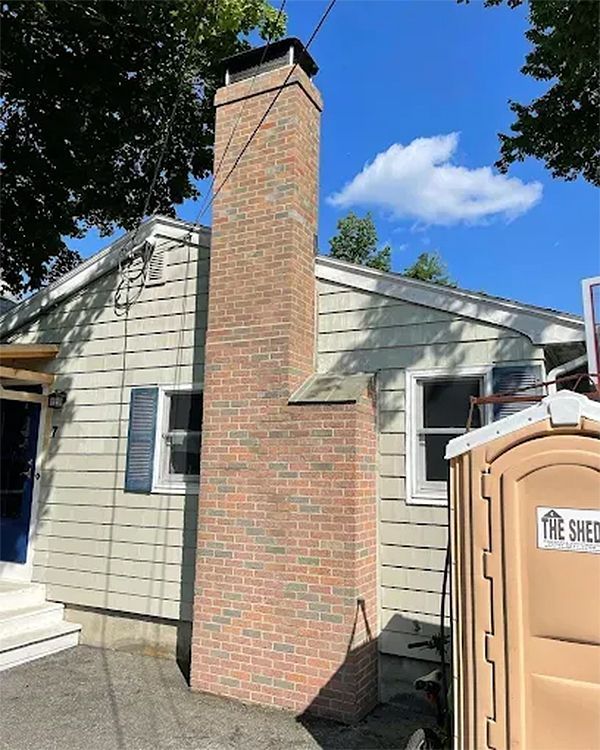 Brick chimney on the side of a house next to a portable toilet under a blue sky.
