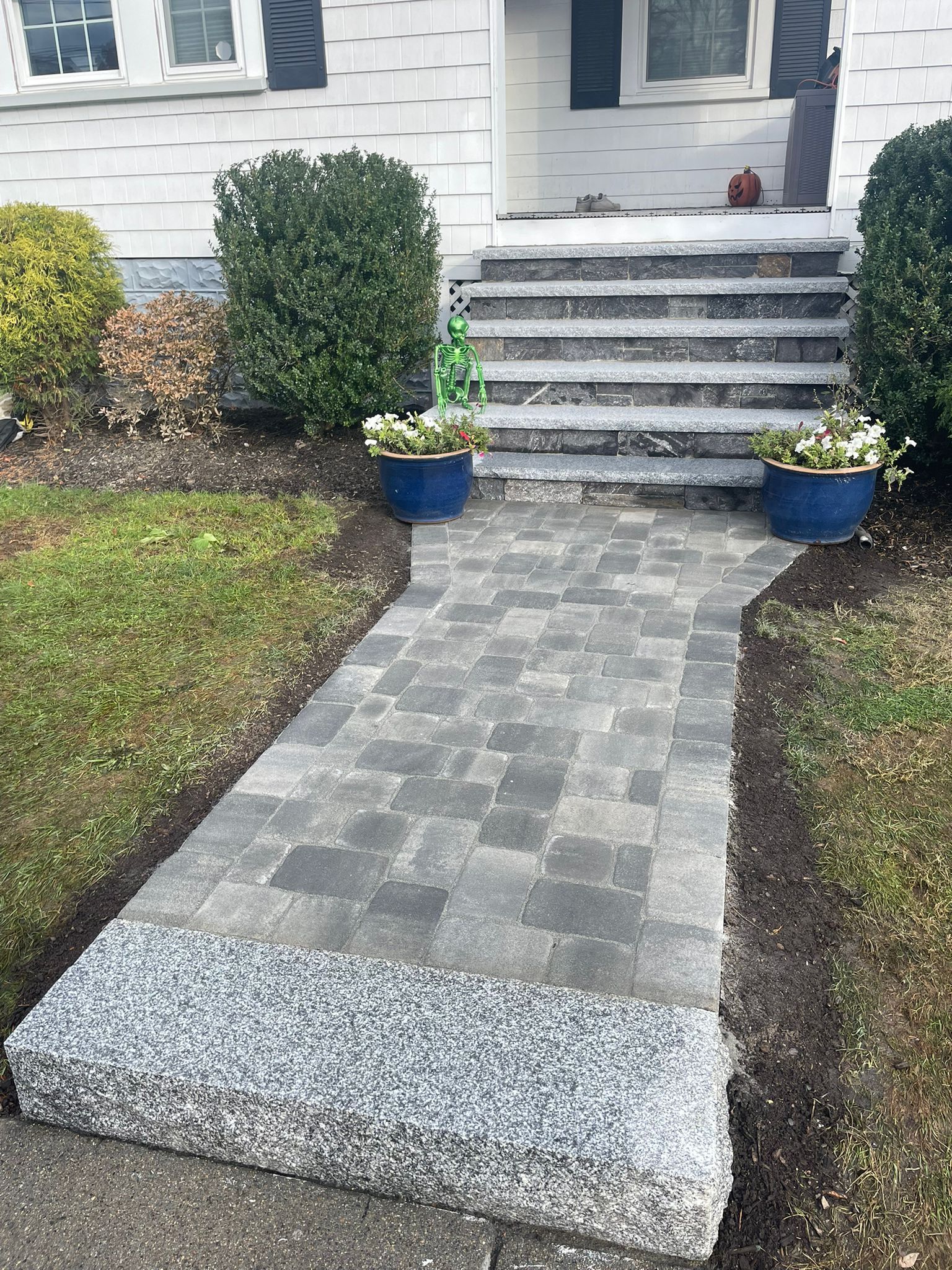 Brick path in herringbone pattern, bordered by green and white-edged plants, running through a garden.