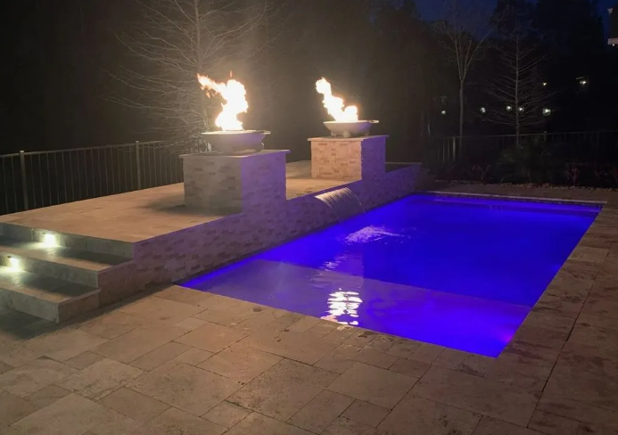 Nighttime pool with blue lights and fire bowls. Stone patio and steps.