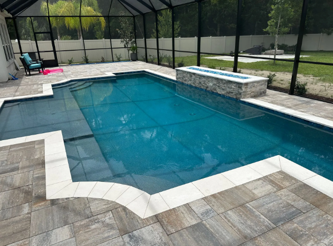 Pool with blue water and stone patio, enclosed by a screen and surrounded by grass.