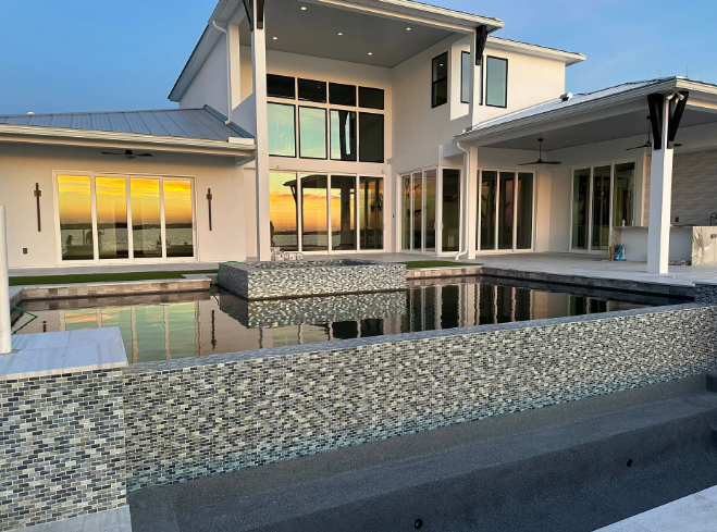 Modern white house with a pool. Sunset reflected in windows and pool water.