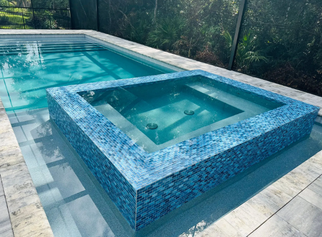 Pool with built-in spa. Blue tiled spa elevated within the larger pool, both filled with clear water.