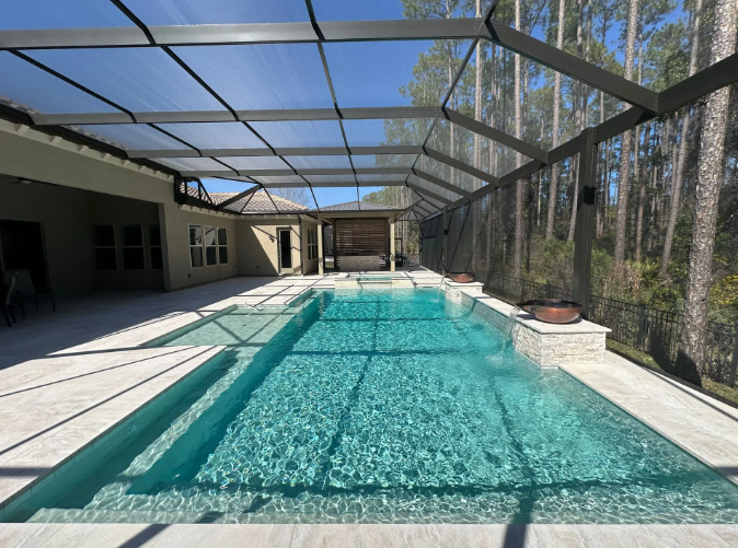 Pool with screened enclosure, bright blue water, beige patio, trees in background.