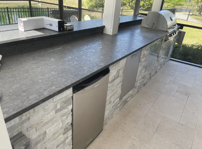 Outdoor kitchen with gray countertops, stainless steel appliances, and stone-veneer facade.