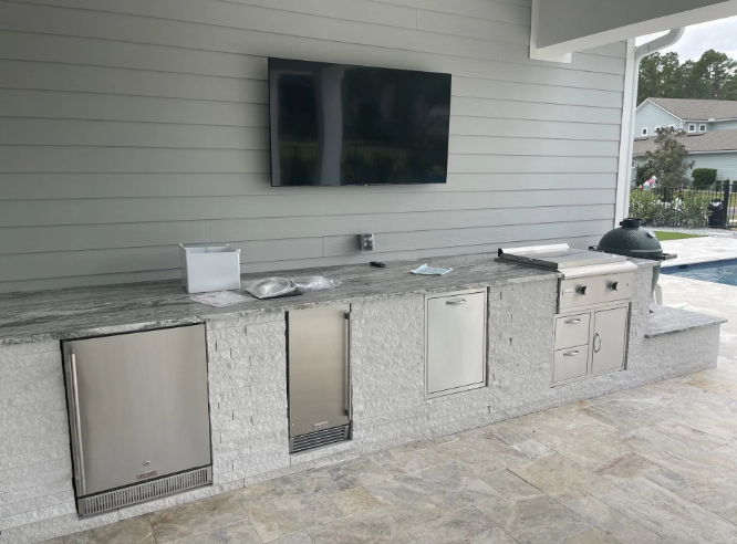 Outdoor kitchen with granite countertop, stainless steel appliances, and mounted TV.