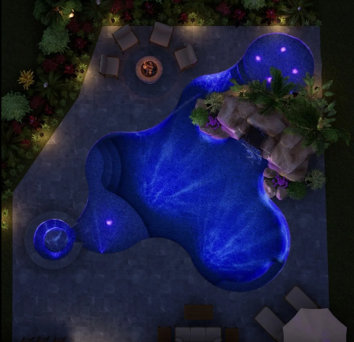 Nighttime aerial view of a blue-lit, uniquely shaped pool with a rock feature, fire pit, and seating.