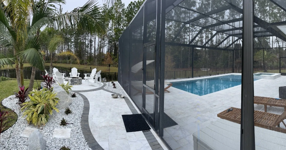 A backyard with a screened-in pool, white patio, landscaping, and a fire pit area.