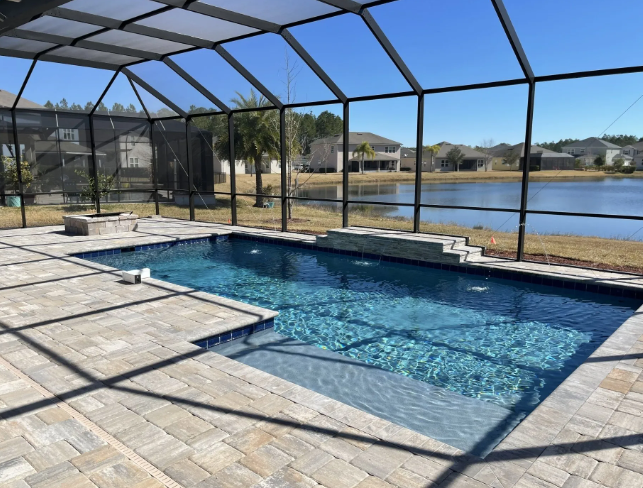 Pool enclosed by black screening, brick patio overlooking a lake, sunny day.