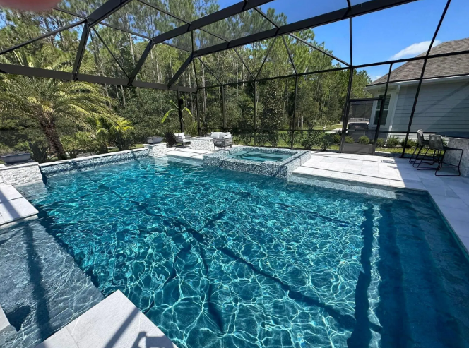 Swimming pool with blue water, surrounded by a white stone patio and enclosed by a screen.