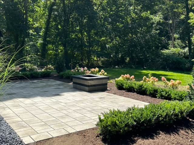 Landscaped patio with stone pavers, flower beds, and trees in a sunny garden