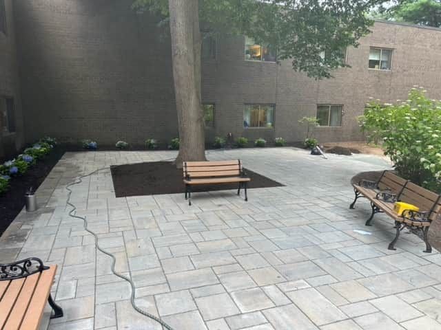 Courtyard with stone pavers, benches around a tree, and a brick apartment building backdrop