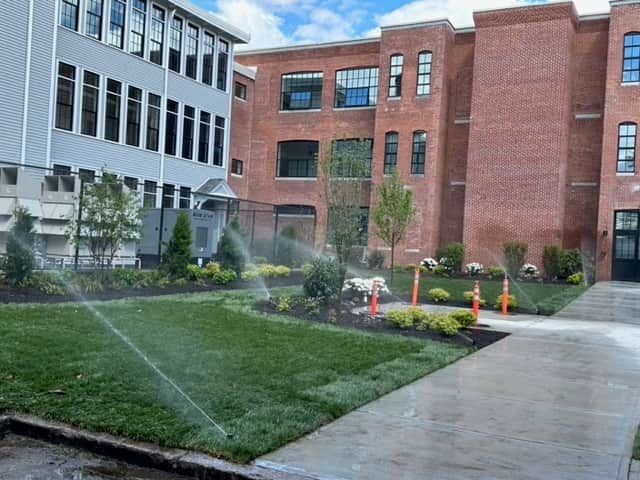 Courtyard with sprinklers watering a lawn beside modern brick and glass buildings