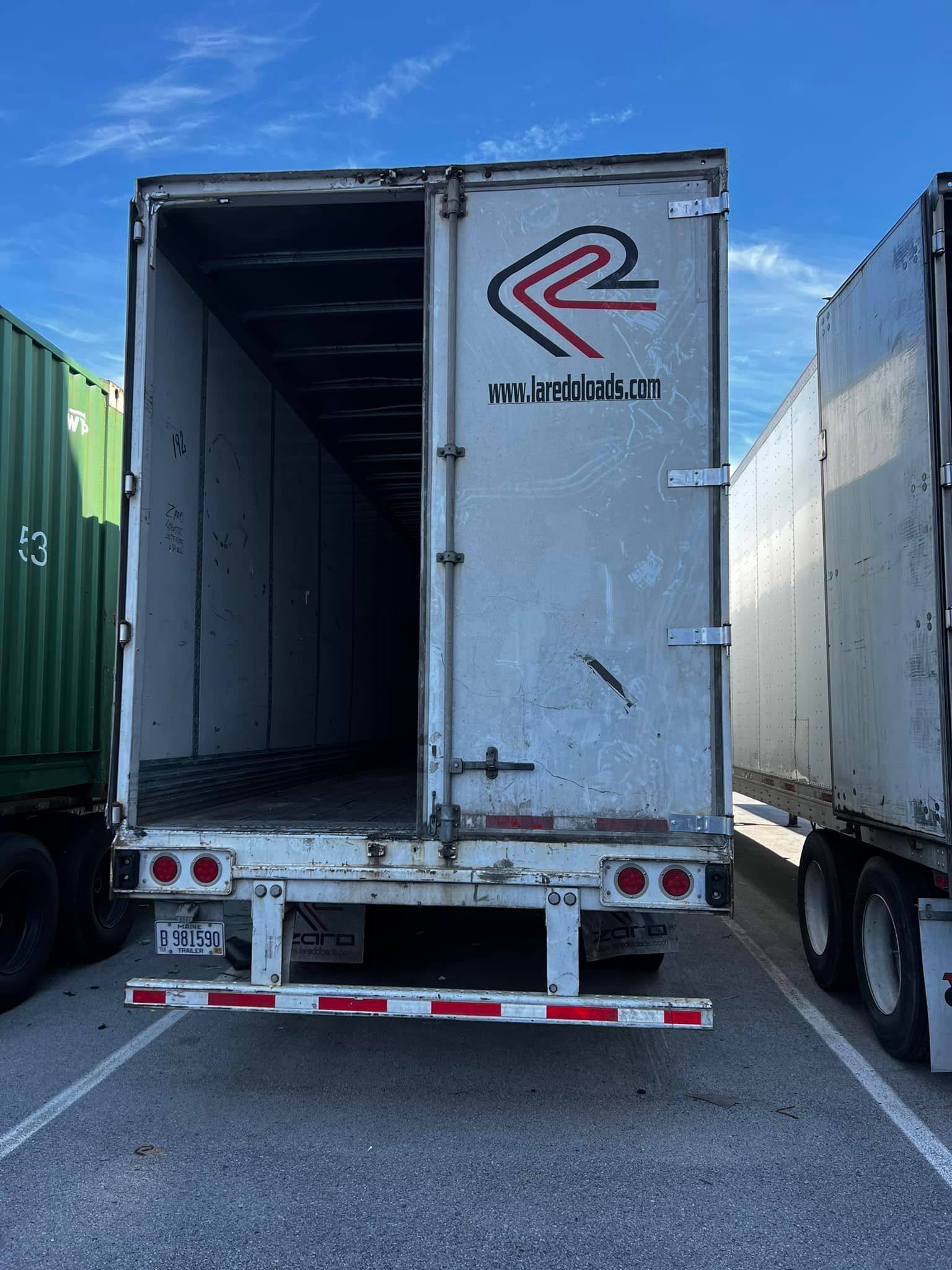 Open, empty semi-trailer with faded logo, parked outdoors on a sunny day.