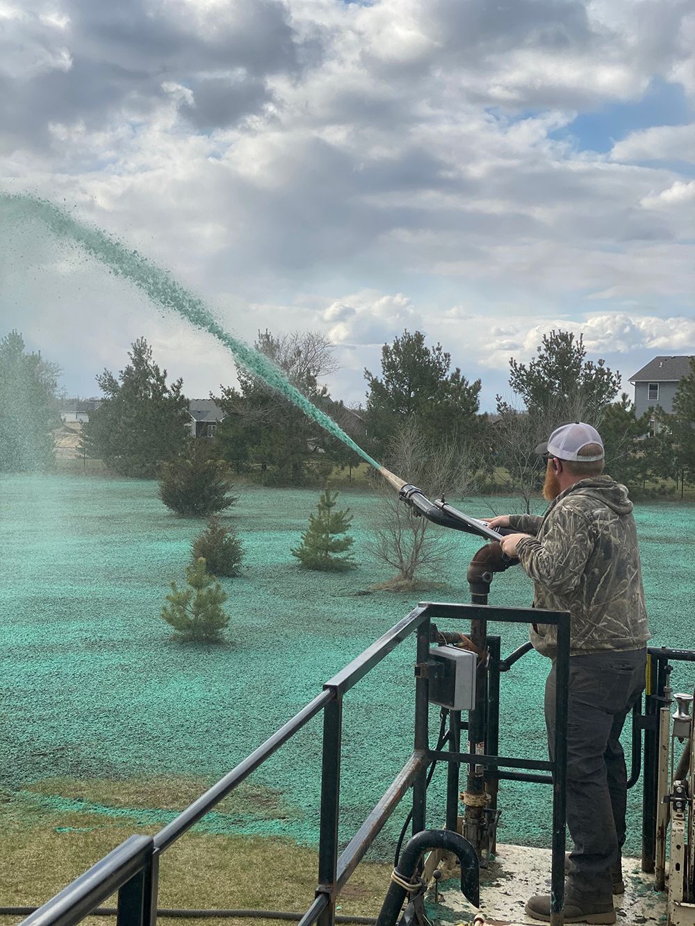 A man is spraying green fertilizer on a lush green field.