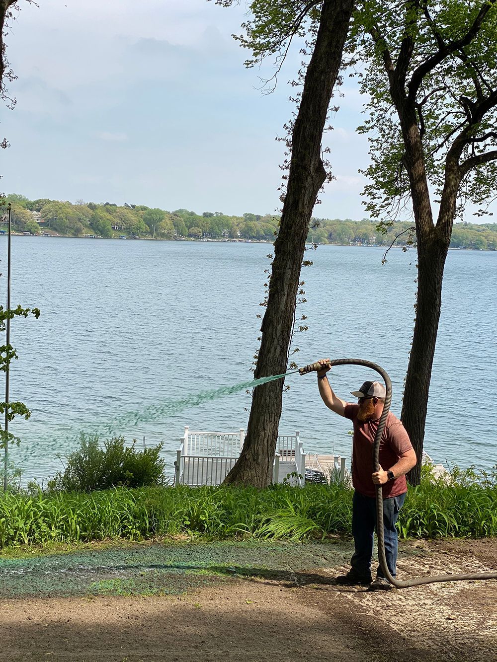 A man is standing next to a lake holding a hose