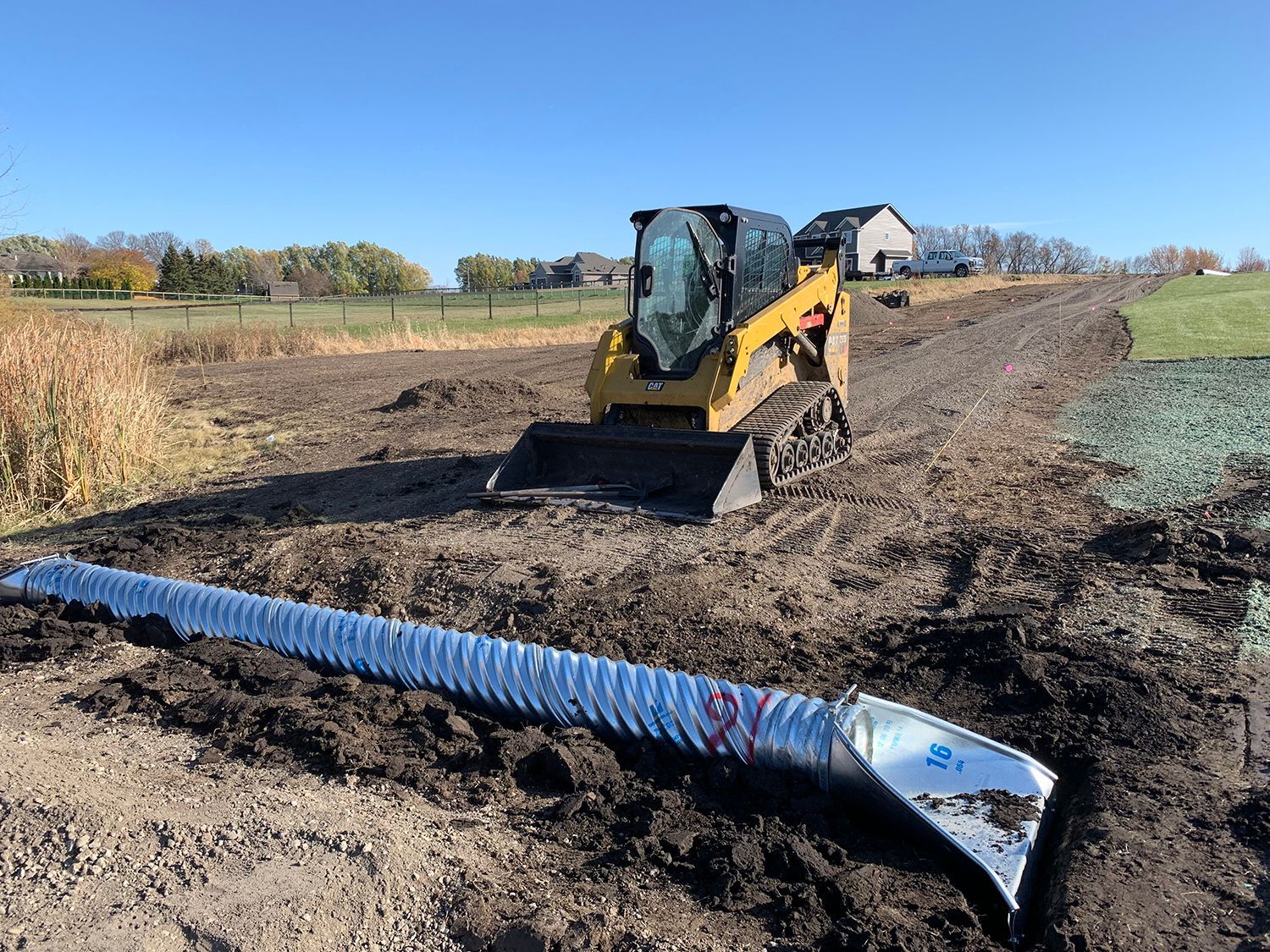 A yellow bulldozer is driving down a dirt road next to a metal pipe