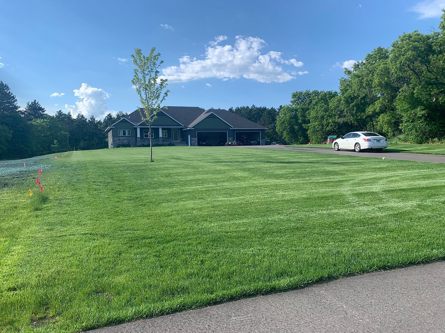 A white car is parked in front of a house on a lush green lawn