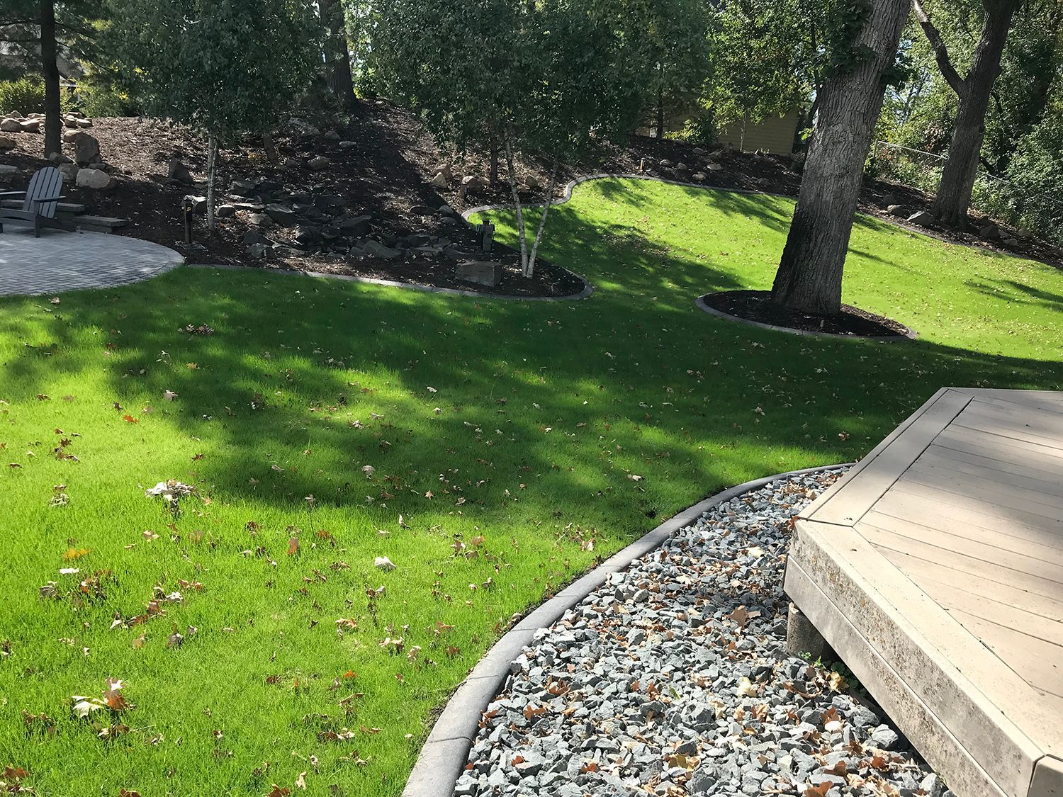 A lush green lawn with trees in the background and a gravel path