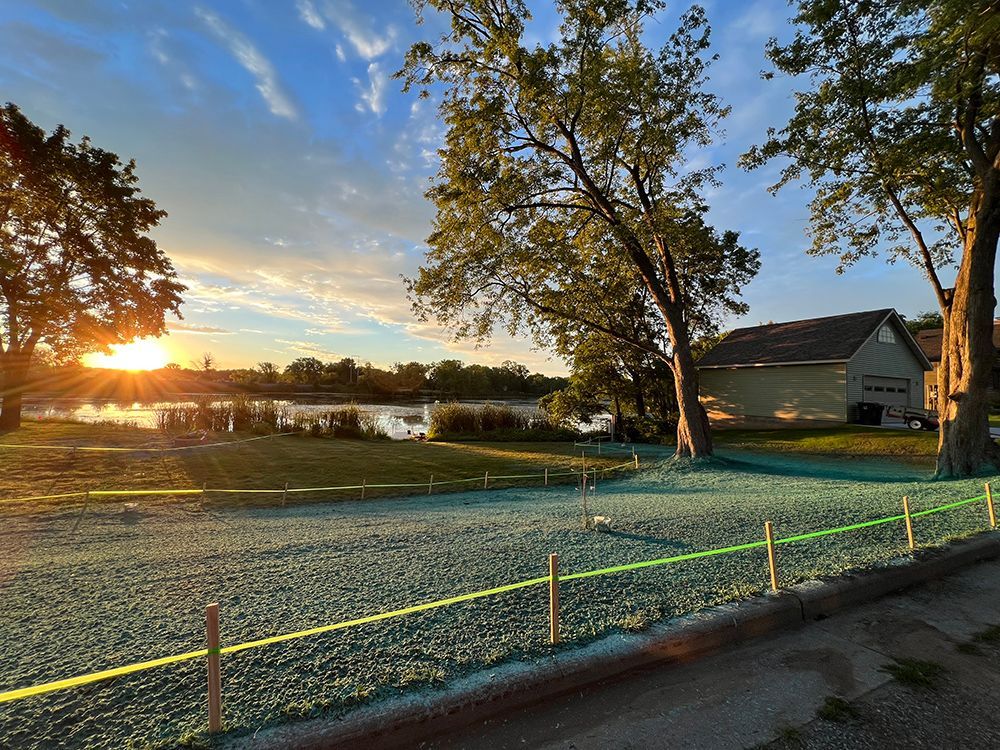 The sun is setting over a lake with a house in the background