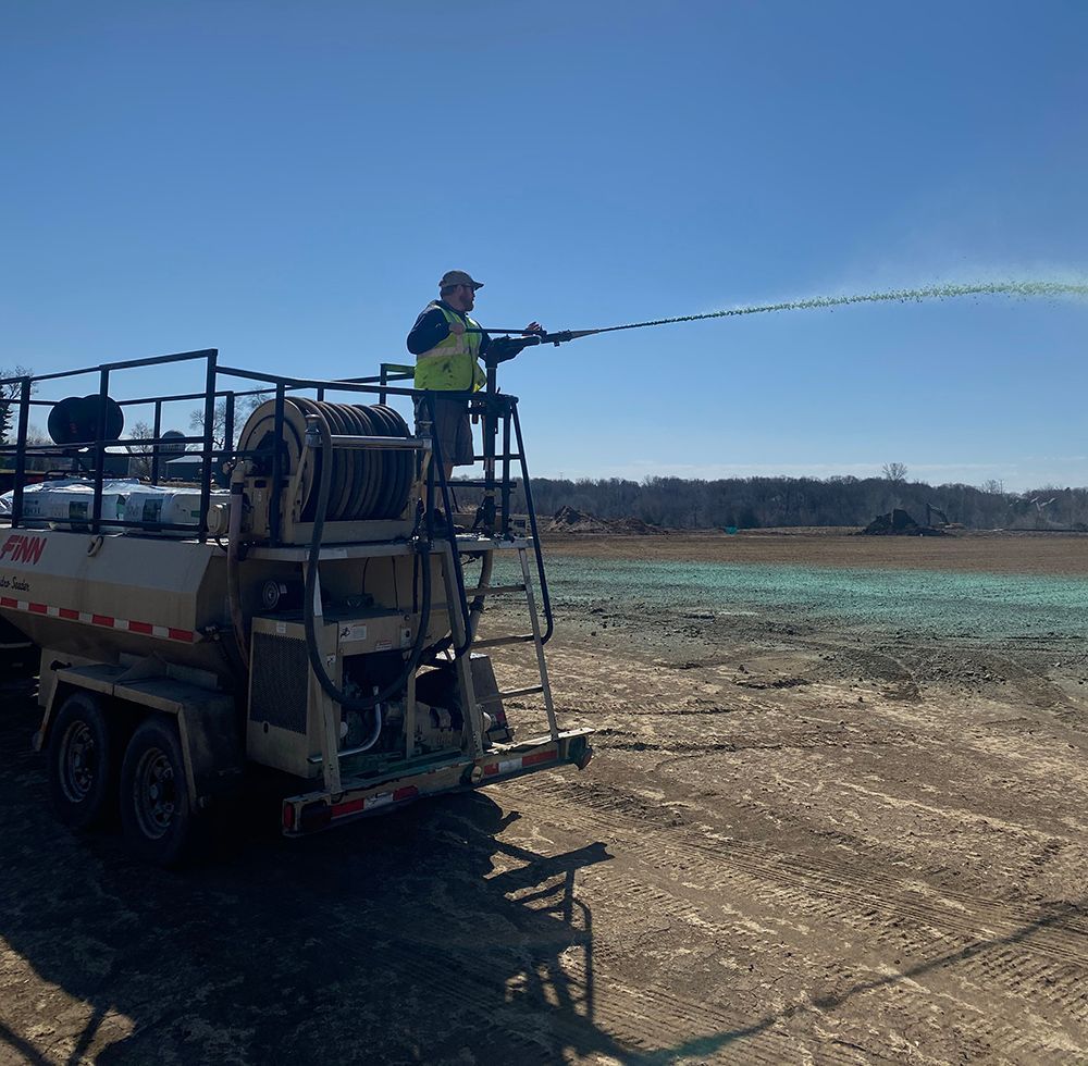 A man is spraying a field with a hose from the back of a truck